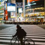 Man on bicycle crosses busy shibuya street at night