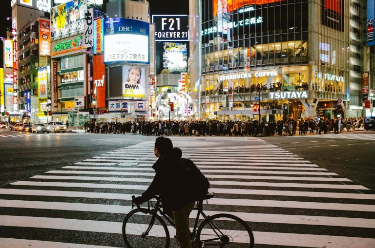 Man on bicycle crosses busy shibuya street at night